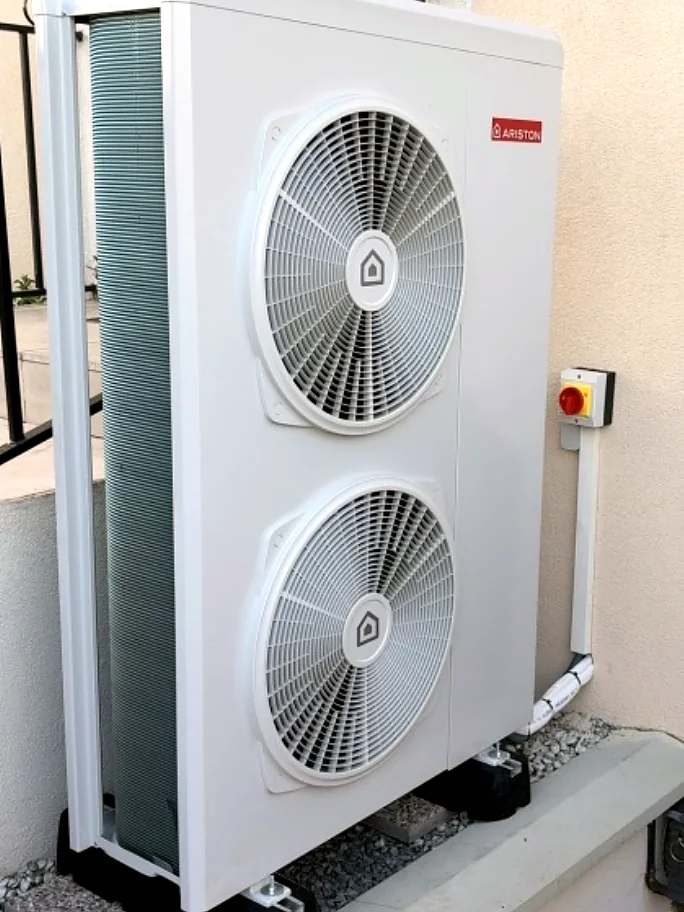 Unité extérieure de pompe à chaleur Ariston à deux ventilateurs, posée sur plots le long d'une façade