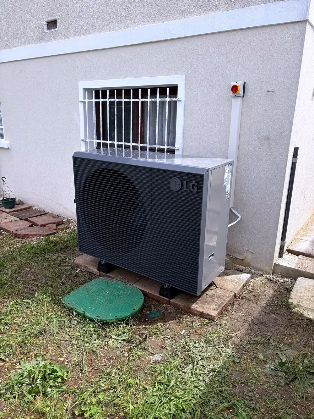 Unité extérieure de pompe à chaleur LG posée sur plots devant une façade en crépi